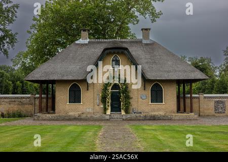 Une charmante maison en briques avec un toit de chaume, des fenêtres cintrées, et une porte verte couverte de plantes grimpantes. La maison se trouve dans un jardin luxuriant, avec un cobb Banque D'Images