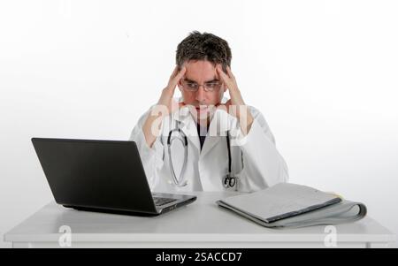 Admin médical : Docteur frustré. Un médecin assis à son bureau regardant son ordinateur la tête dans les mains, isolé sur blanc. Banque D'Images