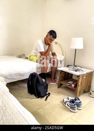 Jeune homme assis sur un lit et utilisant un téléphone portable à Depressa, Italie Banque D'Images