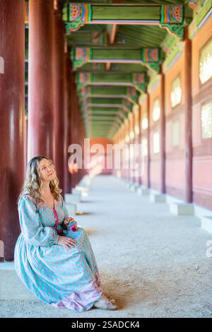Un touriste dans une robe fluide et à motifs est assis paisiblement sur le sol d'un temple traditionnel et animé de Séoul, entouré de p en bois magnifiquement sculpté Banque D'Images