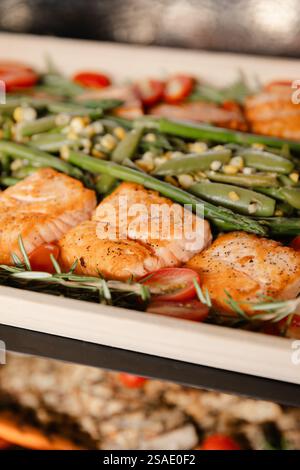 Un plateau magnifiquement agencé présente du saumon grillé garni d'herbes, des haricots verts éclatants et des tomates cerises mûres, parfaites pour un di Banque D'Images