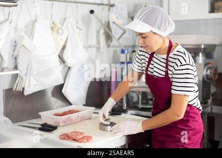 Cuisson des produits semi-finis - fille prépare les côtelettes de viande à l'aide de dispositifs spéciaux Banque D'Images