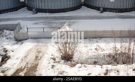 Portail en métal sécurisant les silos industriels derrière une clôture en béton recouverte de neige, créant une scène hivernale sombre dans un paysage rural Banque D'Images