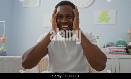 Jeune homme posant joyeusement dans une chambre confortable avec un berceau pour bébé, mettant en valeur le bonheur et le confort dans un cadre intérieur chaleureux. Banque D'Images