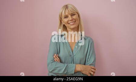 Femme debout sur fond rose, montrant une belle femme caucasienne blonde d'âge moyen avec un sourire chaud, portant une chemise vert clair, isolez Banque D'Images