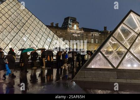 Les visiteurs se tiennent en ligne avec des parapluies entre les pyramides de verre du Louvre, en attendant l'entrée au musée de Paris, en France. Banque D'Images