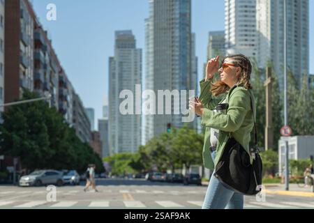 Jeune femme d'affaires traversant la rue tenant un café et se protégeant du soleil à puerto madero, un quartier moderne et populaire touri Banque D'Images