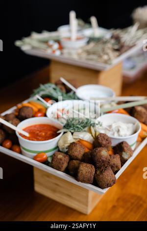 Une sélection magnifiquement arrangée de hors-d'œuvre présente des boules de falafel, des trempettes maison et des légumes frais sur une table en bois lors d'un rassemblement décontracté Banque D'Images