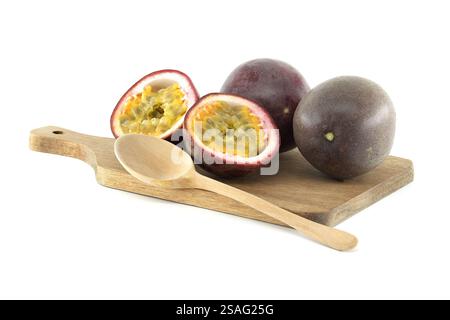 Deux fruits de la passion entiers et deux fruits de la passion coupés en deux, accompagnés d'une cuillère en bois, reposant sur une petite planche à découper contre une grotte blanche propre Banque D'Images