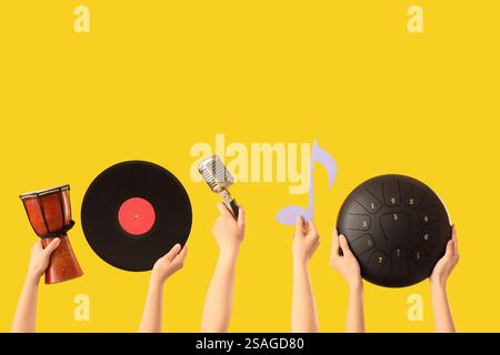 Mains féminines tenant tambour avec vinyle, microphone et glucophone sur fond jaune Banque D'Images