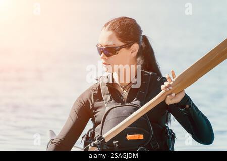 Kayak femme Paddle Water Sports - jeune femme kayak sur l'eau avec paddle à la main, portant des lunettes de soleil et gilet de sauvetage, profitant du plein air. Banque D'Images