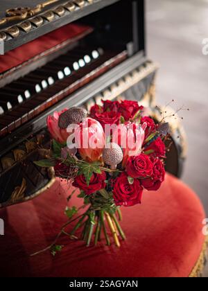 Élégant bouquet de mariage avec des roses rouges et des fleurs exotiques Protea sur Piano Vintage orné Banque D'Images