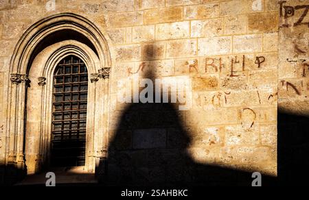 Un mur de pierre avec une fenêtre voûtée et des détails complexes, projetant une ombre qui ressemble à une figure. La texture du mur est rugueuse, avec inscr faible Banque D'Images