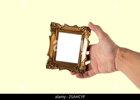 Main masculine tenant un mini cadre doré vintage isolé sur fond jaune Banque D'Images