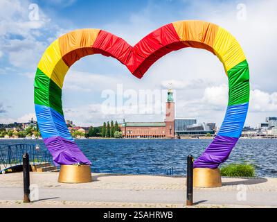 L'hôtel de ville vu à travers une structure en forme de cœur recouverte de tissu aux couleurs du drapeau arc-en-ciel à Stockholm, en Suède, par une journée d'été ensoleillée. Banque D'Images
