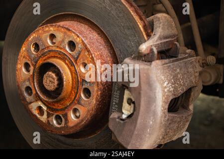 Ancien disque de frein avant avec étrier et plaquettes de frein dans la voiture, sur un ascenseur de voiture dans un atelier, gros plan d'un étrier de frein Banque D'Images
