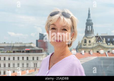 Dame élégante en blouse violette pose à l'extérieur avec paysage urbain Banque D'Images