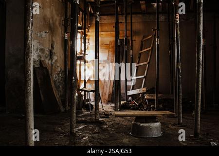 Chantier de construction abandonné avec des poteaux en métal rouillé et des planches en bois : un intérieur sombre et graveleux avec des débris dispersés et Une échelle cassée dans Un Banque D'Images