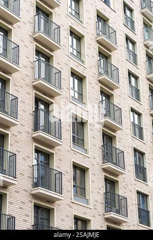 Bâtiment résidentiel moderne avec balcons répétitifs, garde-corps en métal et façade en briques. Concept de logement urbain sur un extérieur lumineux Banque D'Images