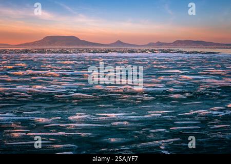 Fonyod, Hongrie - vue panoramique sur le lac Balaton gelé par un après-midi froid d'hiver avec des lumières dorées de coucher de soleil et la montagne Badacsony en arrière-plan Banque D'Images