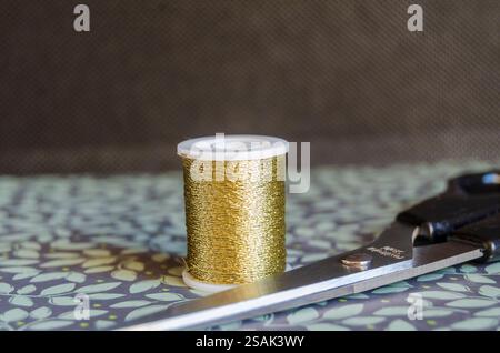 bobine de fil métallique doré et ciseaux sur un fond floral vert Banque D'Images