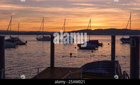 Un coucher de soleil serein sur une rivière calme, avec des teintes orange et rose vibrantes dans le ciel. Un petit voilier est ancré dans l'eau, reflétant le coloré Banque D'Images