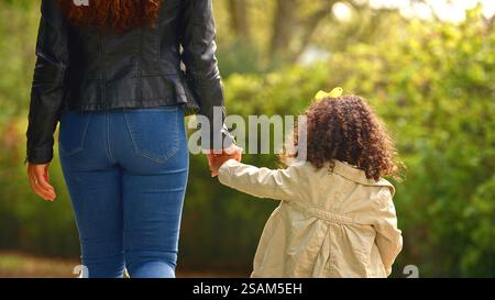 Vue arrière de la mère tenant la main de sa fille marchant à travers les arbres dans la campagne ensemble Banque D'Images