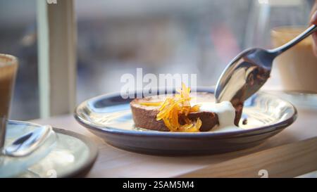 Gros plan d'une personne mangeant du Brownie au chocolat assise sur le siège du hublot du café Banque D'Images