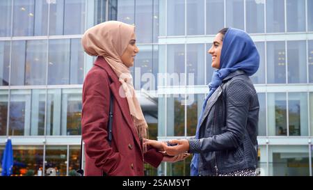 Deux amies britanniques musulmanes portant des hijabs se réunissent devant le bureau Banque D'Images