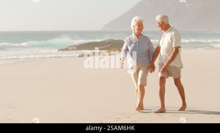 Couple sénior romantique en vacances d'été se tenant la main marchant le long de la plage Banque D'Images