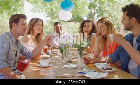 Groupe de jeunes amis multiculturels assis à l'extérieur à table dégustant un gâteau et une boisson chaude ensemble Banque D'Images