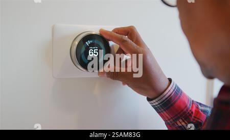 Gros plan de l'homme senior réglant le thermostat de chauffage intelligent numérique à la maison Banque D'Images