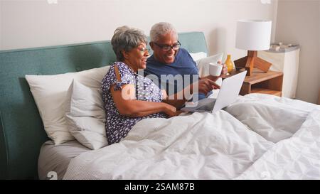 Couple aîné à la maison couché dans le lit passer un appel vidéo avec des parents sur ordinateur portable Banque D'Images