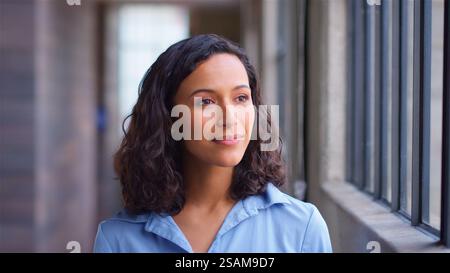 Tête et épaules Portrait de femme d'affaires confiante debout par fenêtre dans le bureau moderne Banque D'Images