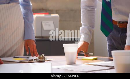 Gros plan de la réunion de l'équipe entreprises debout autour de la table dans le bureau avec des gobelets prenant des notes Banque D'Images