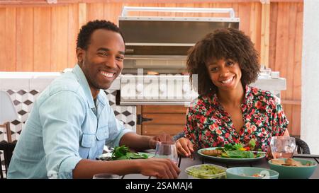 Portrait de jeune couple à l'extérieur à la maison assis à table manger barbecue repas avec salade Banque D'Images