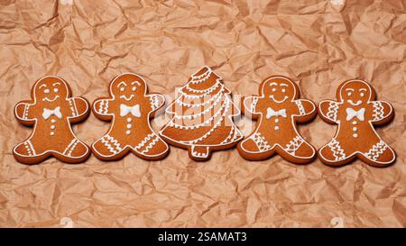 Biscuits festifs en pain d'épices en forme d'hommes et d'arbre, placés sur du papier texturé, vue de dessus. La composition transmet la joie des vacances, un sentiment de communit Banque D'Images