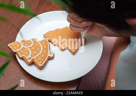 Appliquer à la main du glaçage blanc sur des biscuits en forme de sapin de Noël en pain d'épice. Banque D'Images