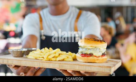 Gros plan sur Male Server avec hamburger et frites dans le bar-restaurant très fréquenté Banque D'Images