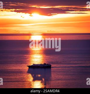 Un coucher de soleil serein sur des eaux calmes avec un bateau naviguant au premier plan. Le ciel est peint dans des teintes vibrantes d'orange et de violet, se reflétant sur le Wat Banque D'Images