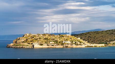 Une vue panoramique sur une île rocheuse avec des ruines, entourée d'eaux calmes sous un ciel nuageux. Le paysage présente des collines en arrière-plan et un cadre serein Banque D'Images