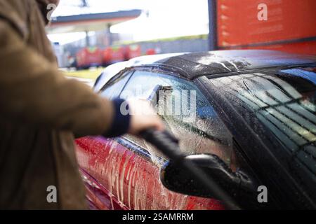 Personne utilisant une brosse pour laver la vitre d'une voiture rouge recouverte de savon Banque D'Images