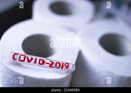 Tube en verre étiqueté COVID-2019 reposant sur des rouleaux de papier toilette blanc Banque D'Images