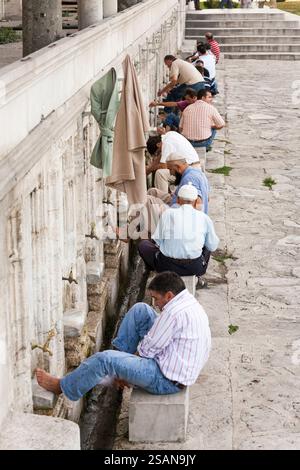 Laver les pieds avant la prière du vendredi à la mosquée : une file d'hommes s'assoit sur des bancs de pierre pour se laver les pieds avant de passer à la mosquée pour prier. Banque D'Images