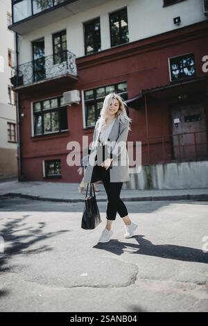 Femme blonde marchant en toute confiance dans un environnement urbain, portant des vêtements décontractés Banque D'Images