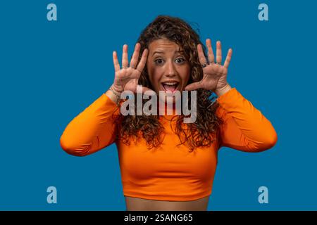 Jeune femme excitée avec les cheveux bouclés montrant dix doigts tout en regardant la caméra sur un fond bleu Banque D'Images