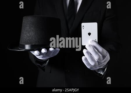 Illusionniste avec carte à jouer et chapeau sur fond noir, gros plan Banque D'Images