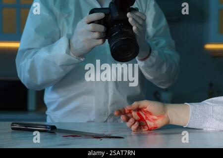 Expert médico-légal avec caméra, couteau, sang et corps de femme morte au comptoir à l'intérieur, gros plan Banque D'Images