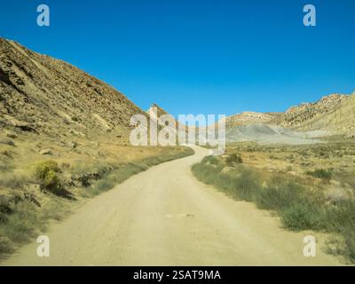 Un chemin de terre serpente à travers un paysage désertique. Le ciel est clair et bleu, et le soleil brille. La route est étroite et sinueuse, et là Ar Banque D'Images