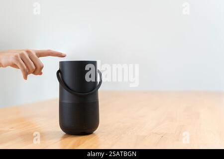 Gros plan de la main appuyant sur un bouton sur une enceinte Bluetooth sans fil entourée d'un fond flou. Se concentrer sur la technologie moderne et l'interaction. E Banque D'Images